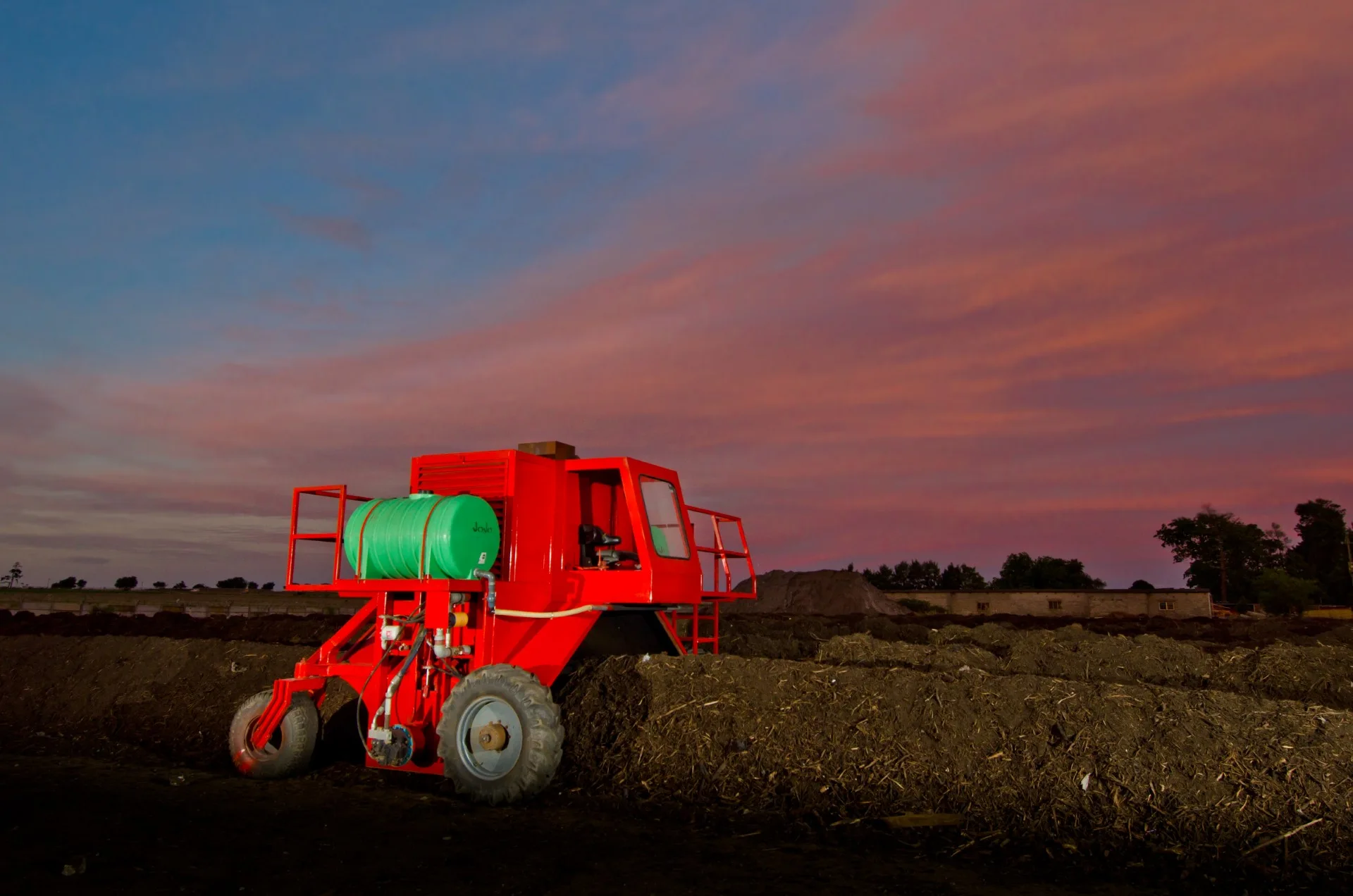 Red compost turner beneath a colourful sunset sky